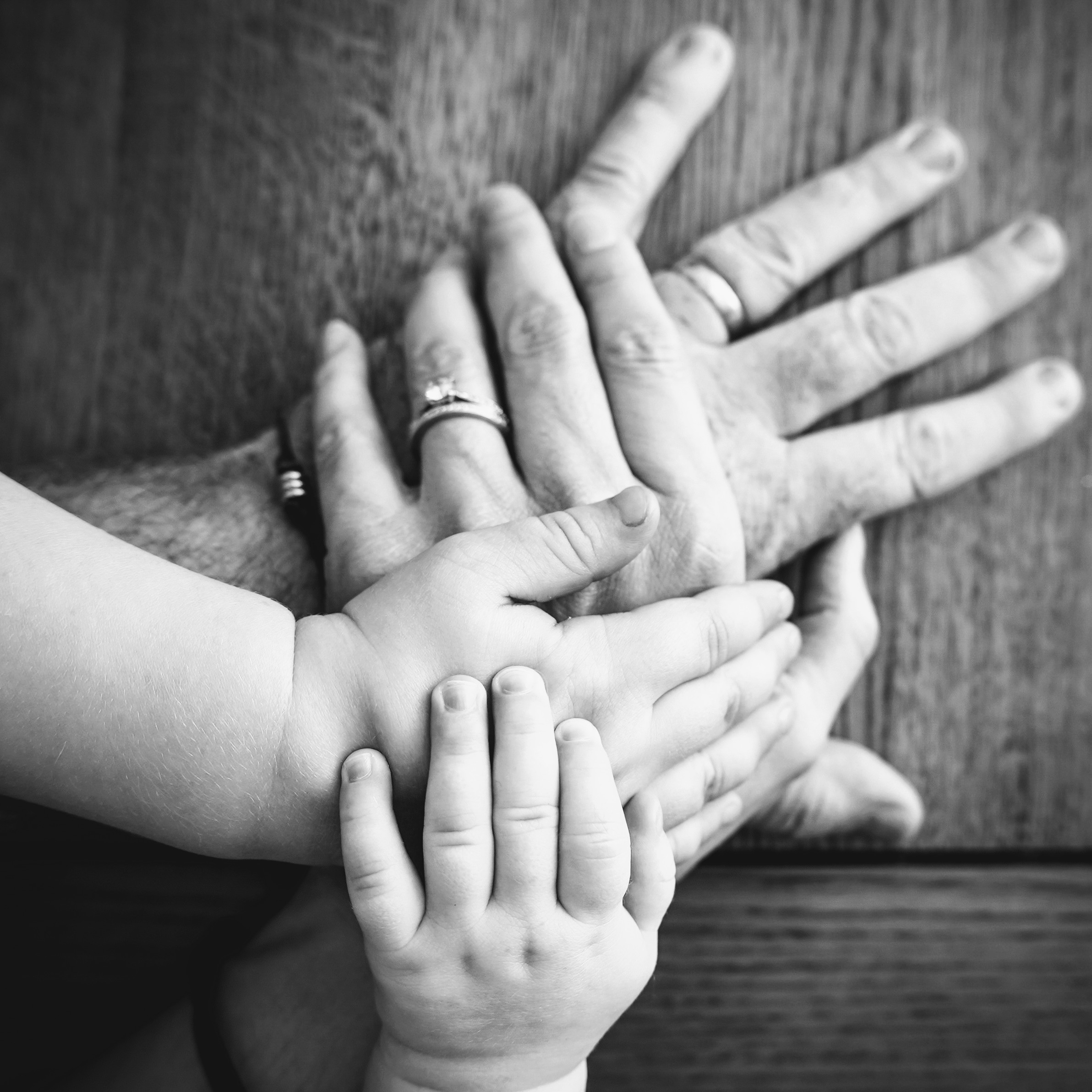 Four hands stacked together on a wooden table: dad's, mum's, a toddler's and a baby's